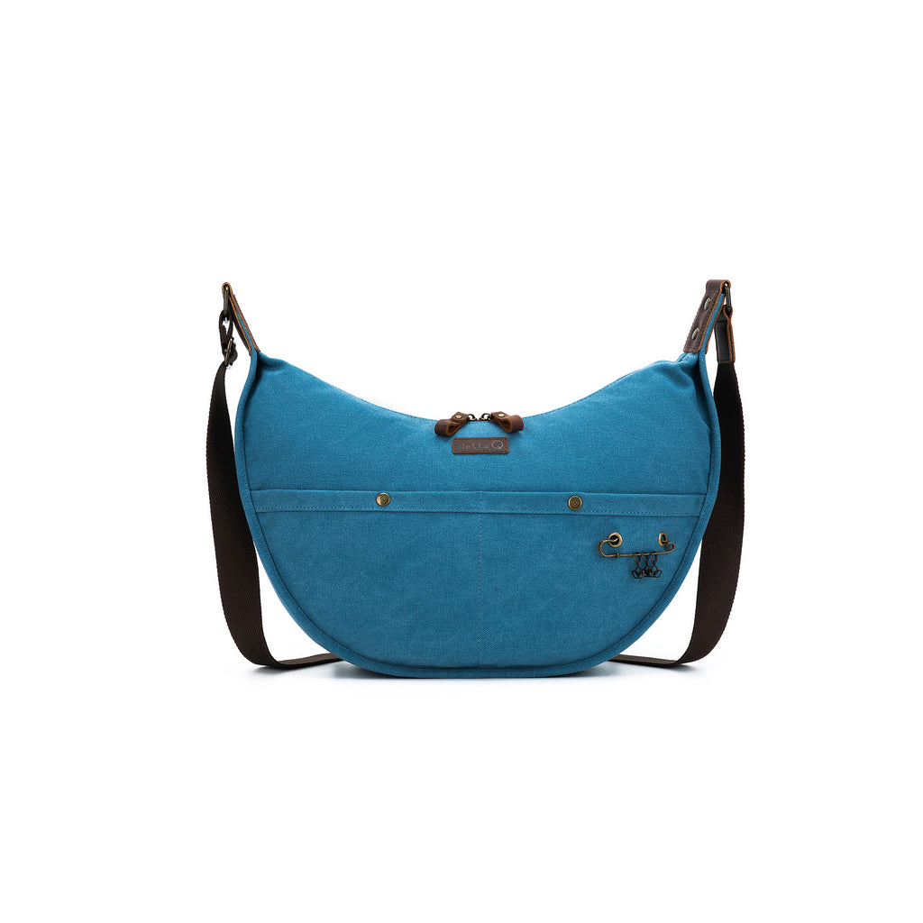 Vibrant teal version of the della Q crescent bag with matching features: front snaps, built-in yarn feeder, leather patch, and brown crossbody strap.